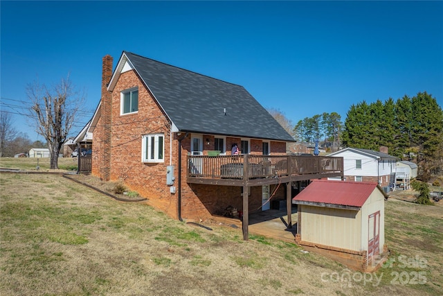 back of house with an outbuilding, brick siding, a chimney, a lawn, and a wooden deck