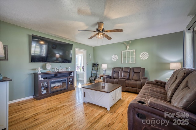 living area with light wood finished floors, baseboards, a ceiling fan, a glass covered fireplace, and a textured ceiling