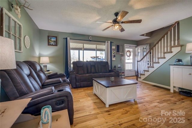 living area with stairs, a textured ceiling, a wealth of natural light, and light wood-style floors