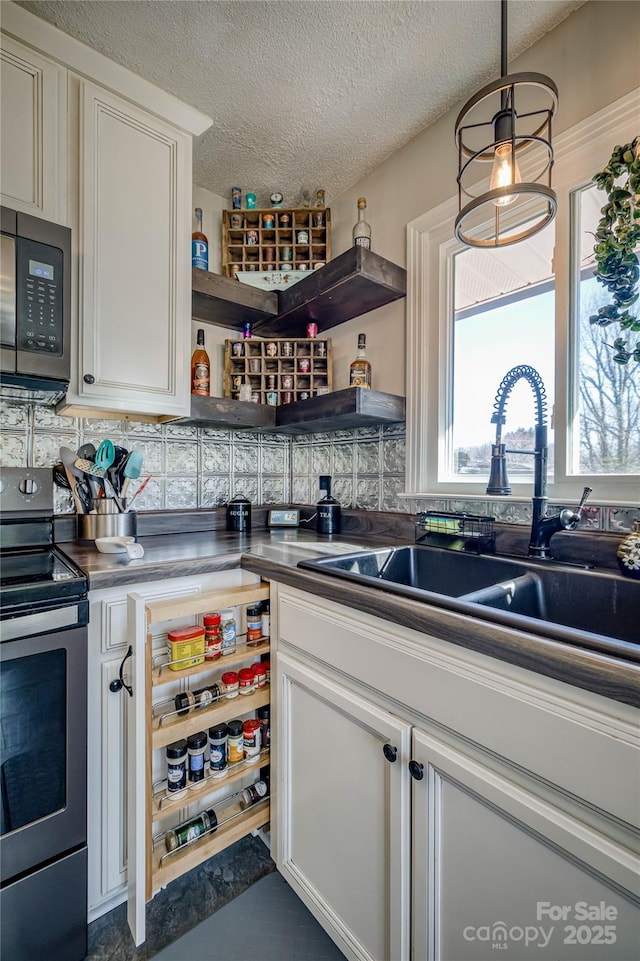 kitchen with black microwave, a sink, stainless steel electric stove, open shelves, and dark countertops