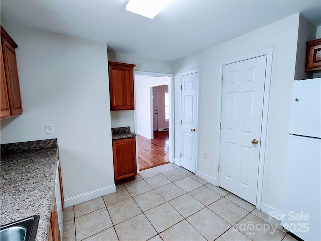 1806 Bringle Ferry Rd, Salisbury, NC 28146 - kitchen featuring light tile patterned floors, baseboards, dark stone counters, freestanding refrigerator, and a sink