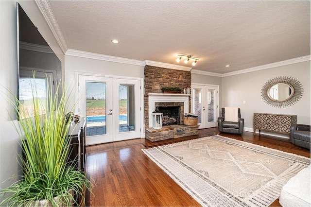 living area with french doors, ornamental molding, wood finished floors, a textured ceiling, and a stone fireplace