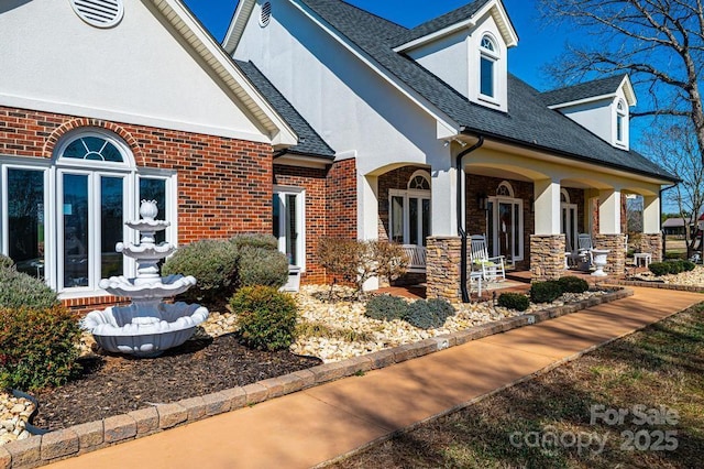 view of side of home with brick siding, roof with shingles, french doors, and stucco siding