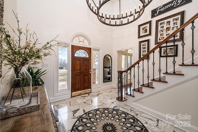 foyer entrance featuring marble finish floor, baseboards, stairway, and a chandelier