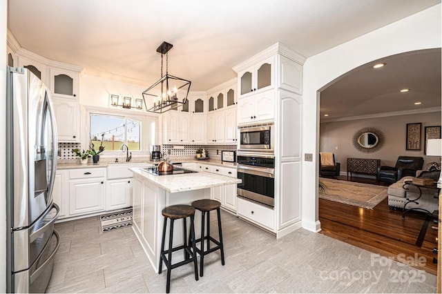 kitchen featuring arched walkways, a breakfast bar area, stainless steel appliances, open floor plan, and glass insert cabinets