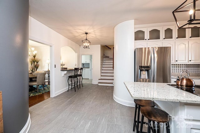 kitchen with a breakfast bar area, an inviting chandelier, white cabinets, light stone countertops, and stainless steel fridge with ice dispenser