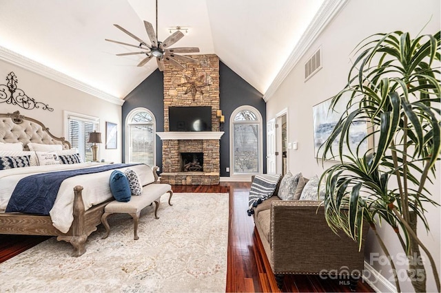 bedroom with crown molding, dark wood finished floors, a stone fireplace, and high vaulted ceiling