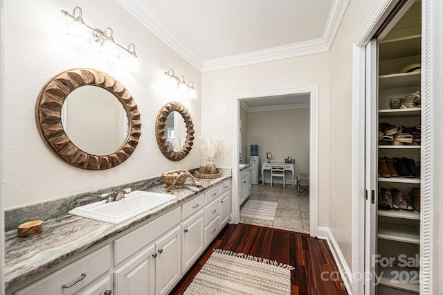 bathroom with baseboards, ornamental molding, wood finished floors, a spacious closet, and vanity