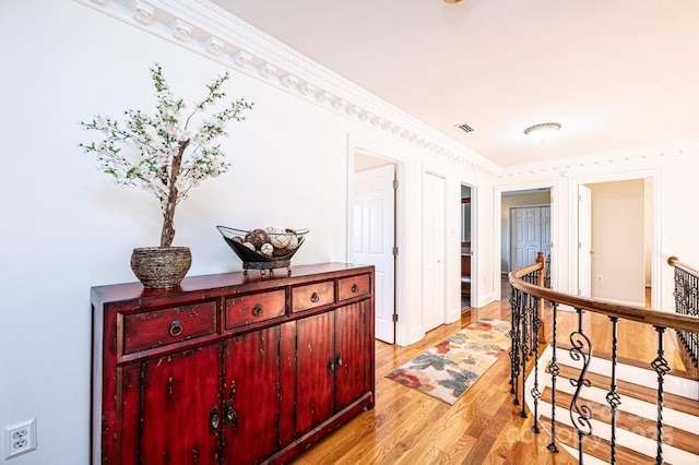 hallway with baseboards, visible vents, ornamental molding, an upstairs landing, and light wood-style floors