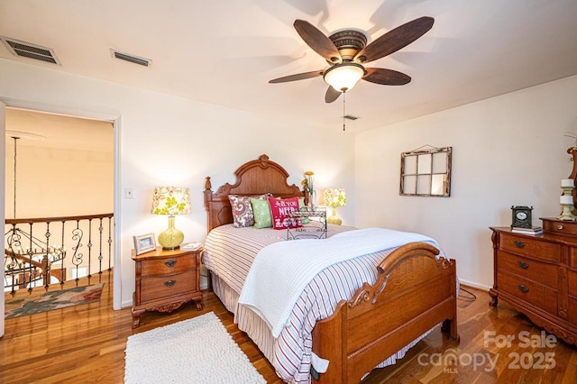 bedroom with a ceiling fan, visible vents, baseboards, and wood finished floors