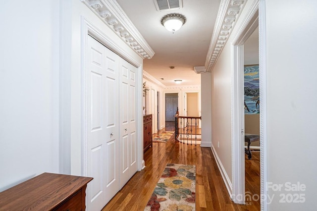 hallway with wood finished floors, an upstairs landing, visible vents, baseboards, and ornamental molding