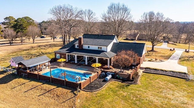 rear view of house with fence, a yard, a fenced in pool, a chimney, and a patio area