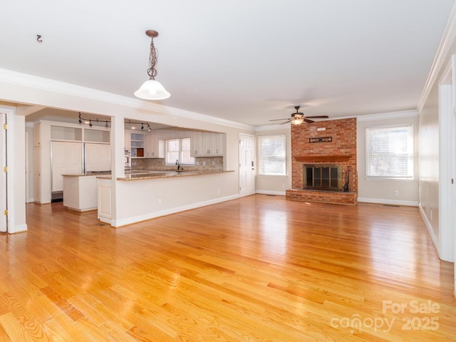 unfurnished living room featuring a sink, a ceiling fan, light wood-style floors, a brick fireplace, and crown molding