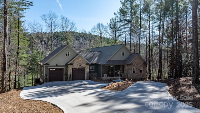 view of front of house with stone siding, concrete driveway, an attached garage, and a forest view