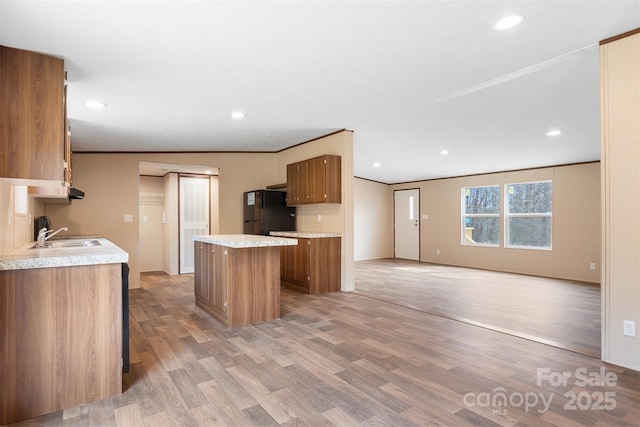 kitchen with a kitchen island, brown cabinets, wood finished floors, freestanding refrigerator, and light countertops