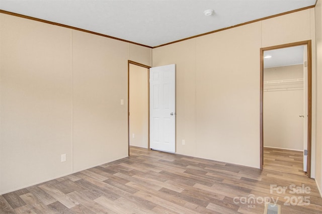 unfurnished bedroom featuring visible vents, ornamental molding, wood finished floors, a walk in closet, and a closet