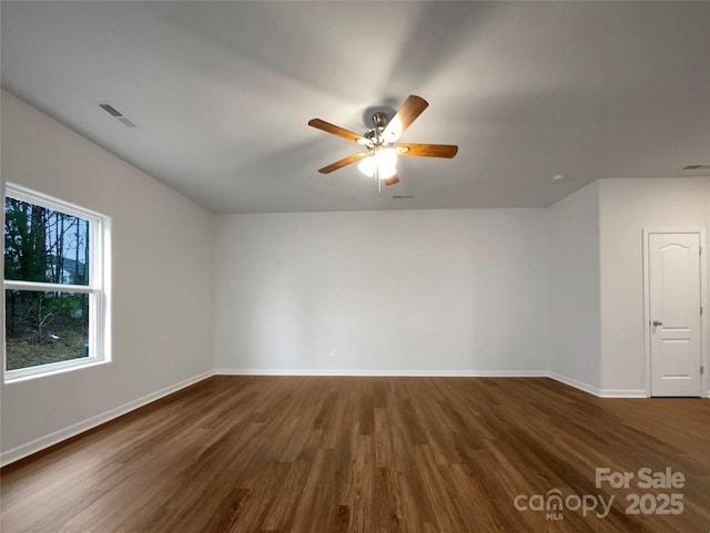 unfurnished room featuring dark wood-type flooring, a ceiling fan, visible vents, and baseboards