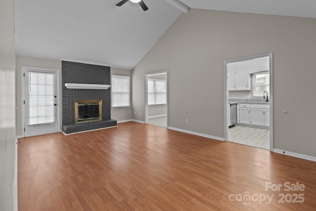 unfurnished living room featuring a sink, a ceiling fan, light wood-type flooring, a brick fireplace, and beamed ceiling