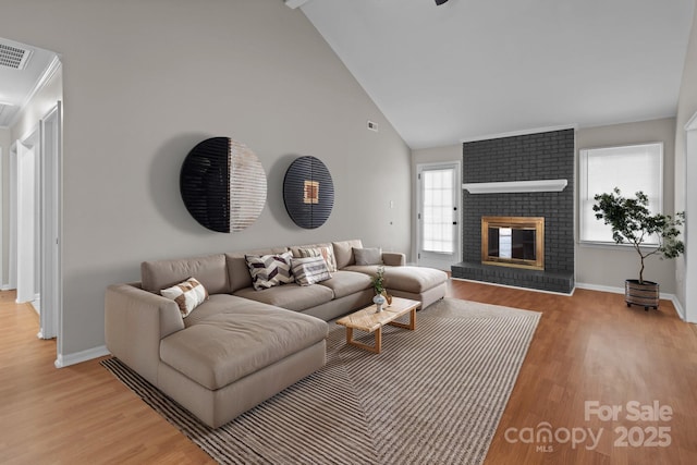 living area with high vaulted ceiling, a brick fireplace, light wood-style flooring, and baseboards