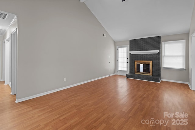 unfurnished living room with high vaulted ceiling, light wood finished floors, a brick fireplace, and baseboards