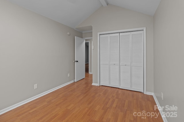 unfurnished bedroom featuring lofted ceiling with beams, a closet, light wood-style flooring, and baseboards