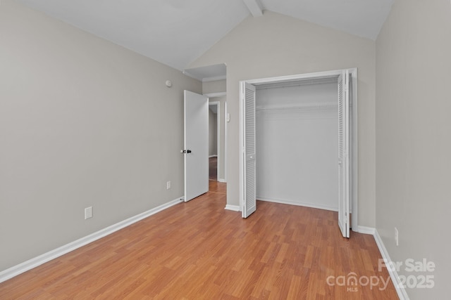 unfurnished bedroom with a closet, baseboards, vaulted ceiling with beams, and light wood finished floors