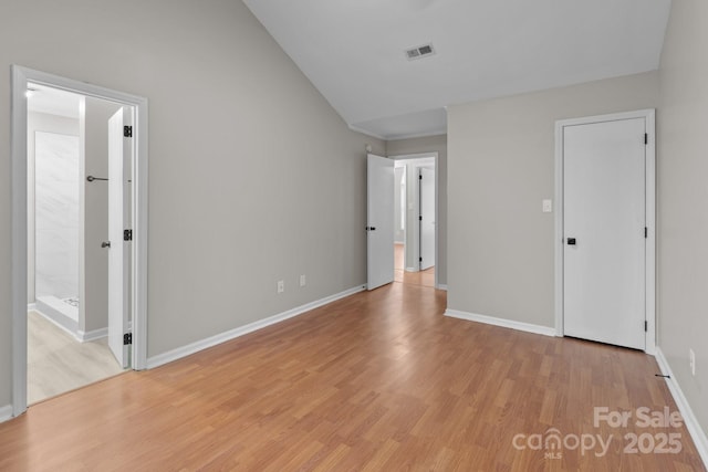 unfurnished bedroom featuring baseboards, lofted ceiling, visible vents, and light wood-style floors