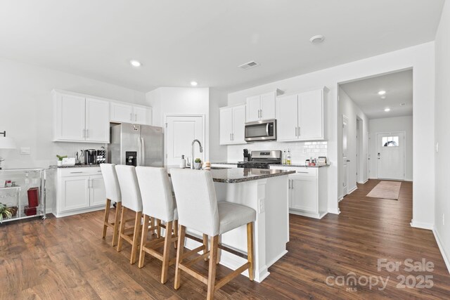 kitchen with white cabinetry, an island with sink, stainless steel appliances, a kitchen bar, and backsplash