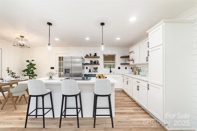 kitchen with light wood-style flooring, a center island, open shelves, stainless steel fridge, and a kitchen bar