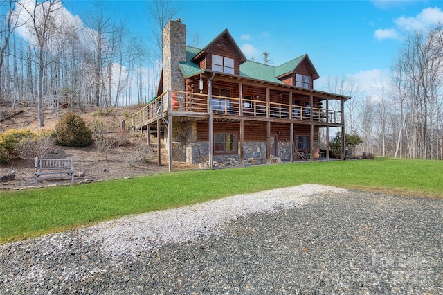 back of house featuring stone siding, a chimney, metal roof, and a yard