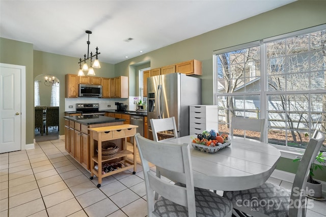 kitchen featuring light tile patterned floors, dark countertops, a center island, decorative light fixtures, and stainless steel appliances