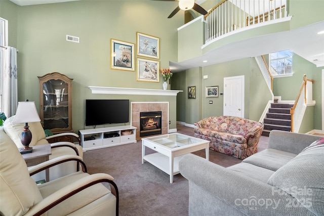 living room featuring ceiling fan, carpet flooring, visible vents, stairway, and a tiled fireplace