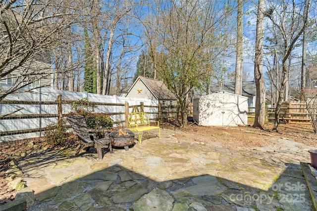 view of patio featuring a fenced backyard, an outdoor structure, a fire pit, and a shed