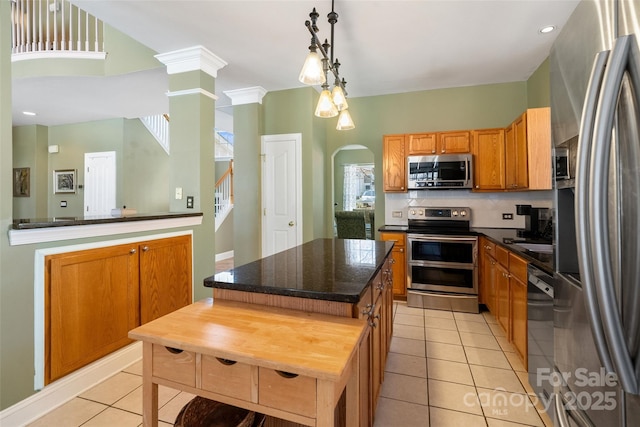 kitchen with a center island, pendant lighting, brown cabinets, stainless steel appliances, and light tile patterned flooring