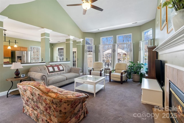 living room with decorative columns, a tiled fireplace, ceiling fan, dark colored carpet, and high vaulted ceiling