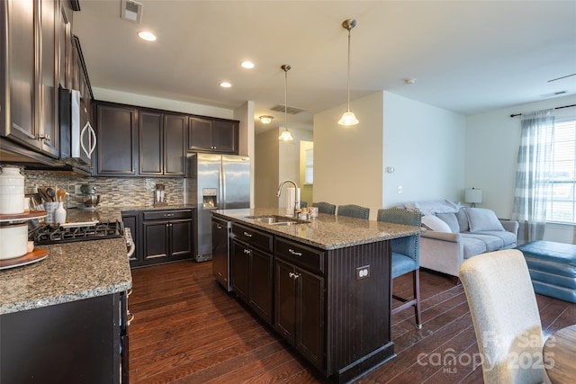 kitchen with light stone counters, decorative light fixtures, visible vents, open floor plan, and an island with sink