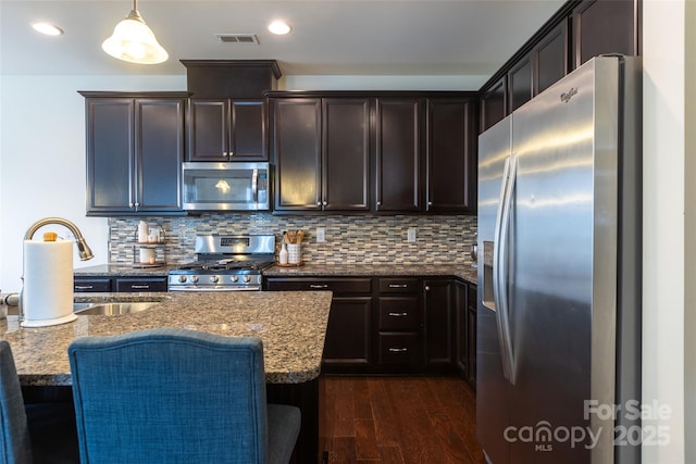 kitchen with light stone counters, a breakfast bar, appliances with stainless steel finishes, backsplash, and pendant lighting