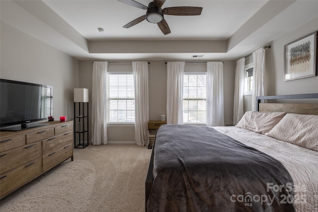 bedroom featuring a tray ceiling, light colored carpet, visible vents, and baseboards