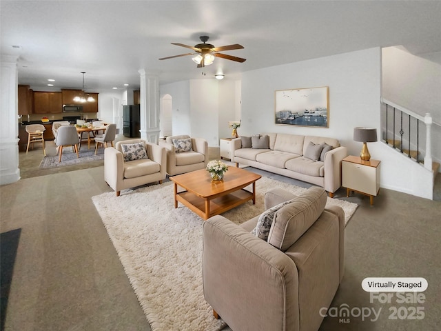 living area with a ceiling fan, decorative columns, and stairs