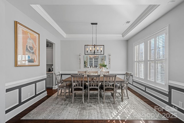 dining space featuring a wainscoted wall, visible vents, a raised ceiling, and crown molding