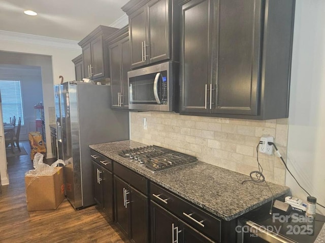 kitchen with stainless steel appliances, dark stone counters, crown molding, and dark wood-style floors