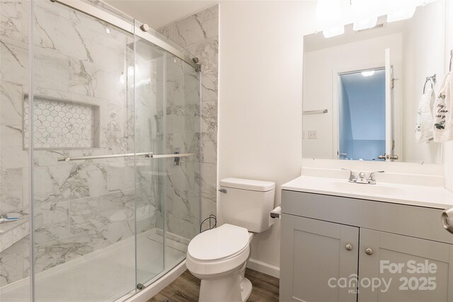 bathroom with wood finished floors, a marble finish shower, and toilet