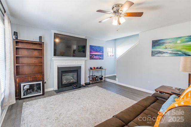 living room with wood finished floors, a fireplace with flush hearth, a ceiling fan, and baseboards