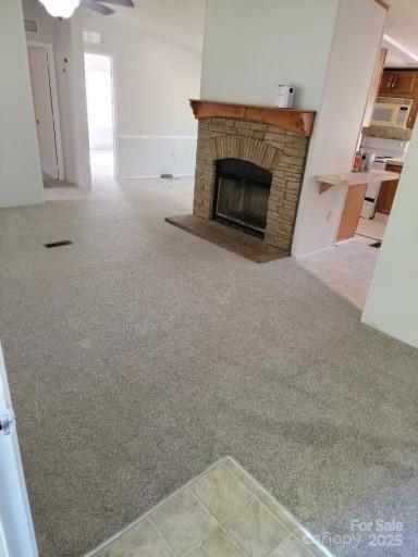 unfurnished living room with light carpet, ceiling fan, a fireplace, and visible vents