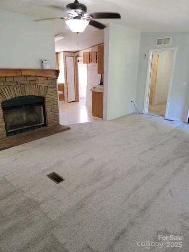 unfurnished living room featuring a brick fireplace, visible vents, a ceiling fan, and light colored carpet