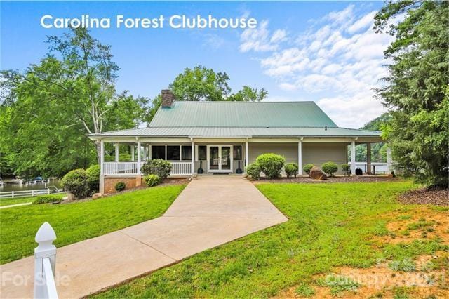 country-style home featuring covered porch, metal roof, a chimney, and a front lawn