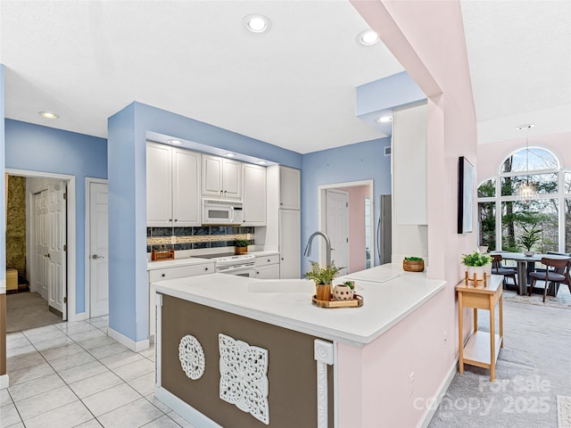 kitchen with tasteful backsplash, light countertops, white cabinets, white appliances, and a peninsula