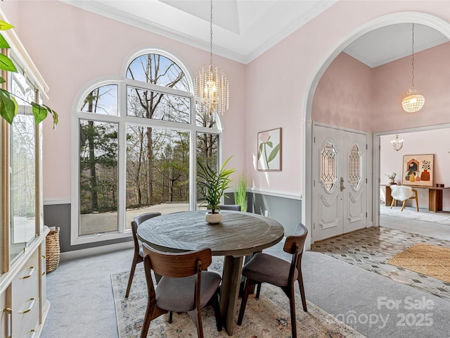 dining room with arched walkways, a notable chandelier, light colored carpet, a high ceiling, and ornamental molding