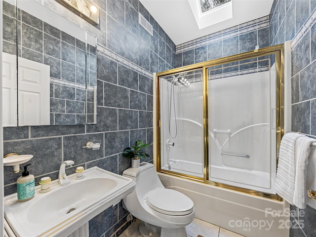 bathroom with toilet, bath / shower combo with glass door, a skylight, a sink, and tile walls