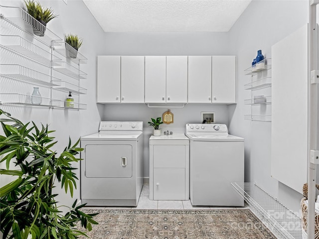 clothes washing area featuring cabinet space, a textured ceiling, washing machine and clothes dryer, and light tile patterned floors